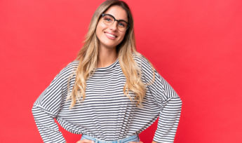 Young Uruguayan woman isolated on red background posing with arms at hip and smiling