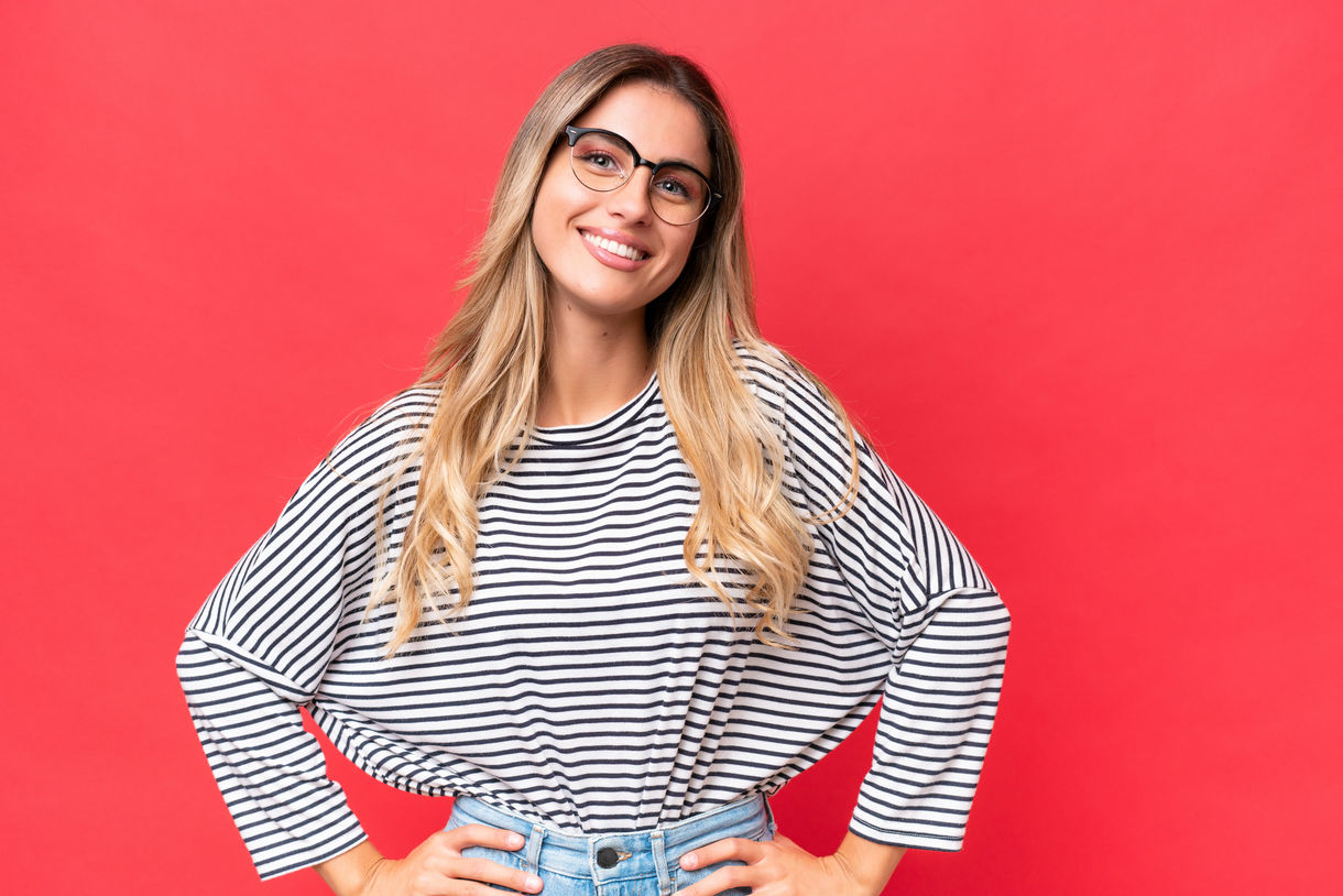 Young Uruguayan woman isolated on red background posing with arms at hip and smiling